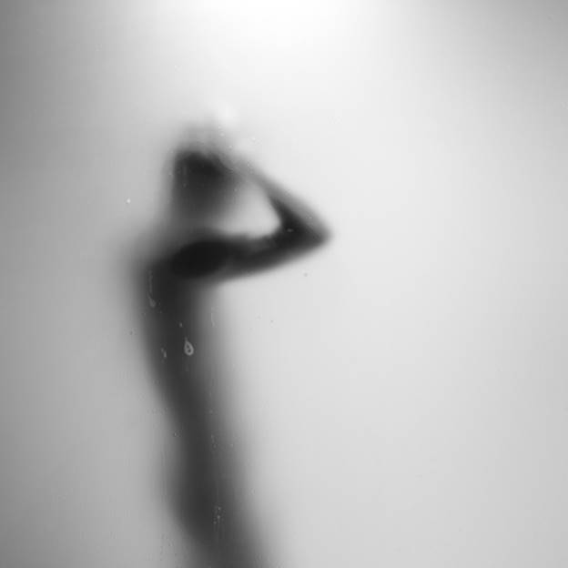 A blurry, black and white photo shows a silhouette of a person behind frosted glass. The person has their arms raised to their head.